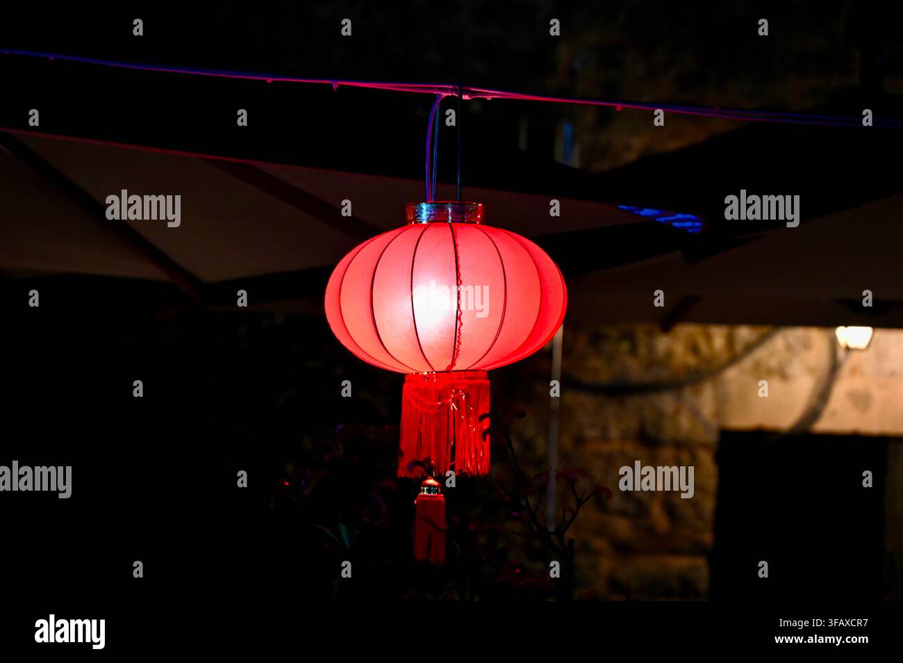 Une photographie nocturne horizontale capturant une lanterne de papier chinoise rouge traditionnelle illuminée suspendue à une corde à l'extérieur, projetant une lumière chaude et festive sur un fond sombre Banque D'Images