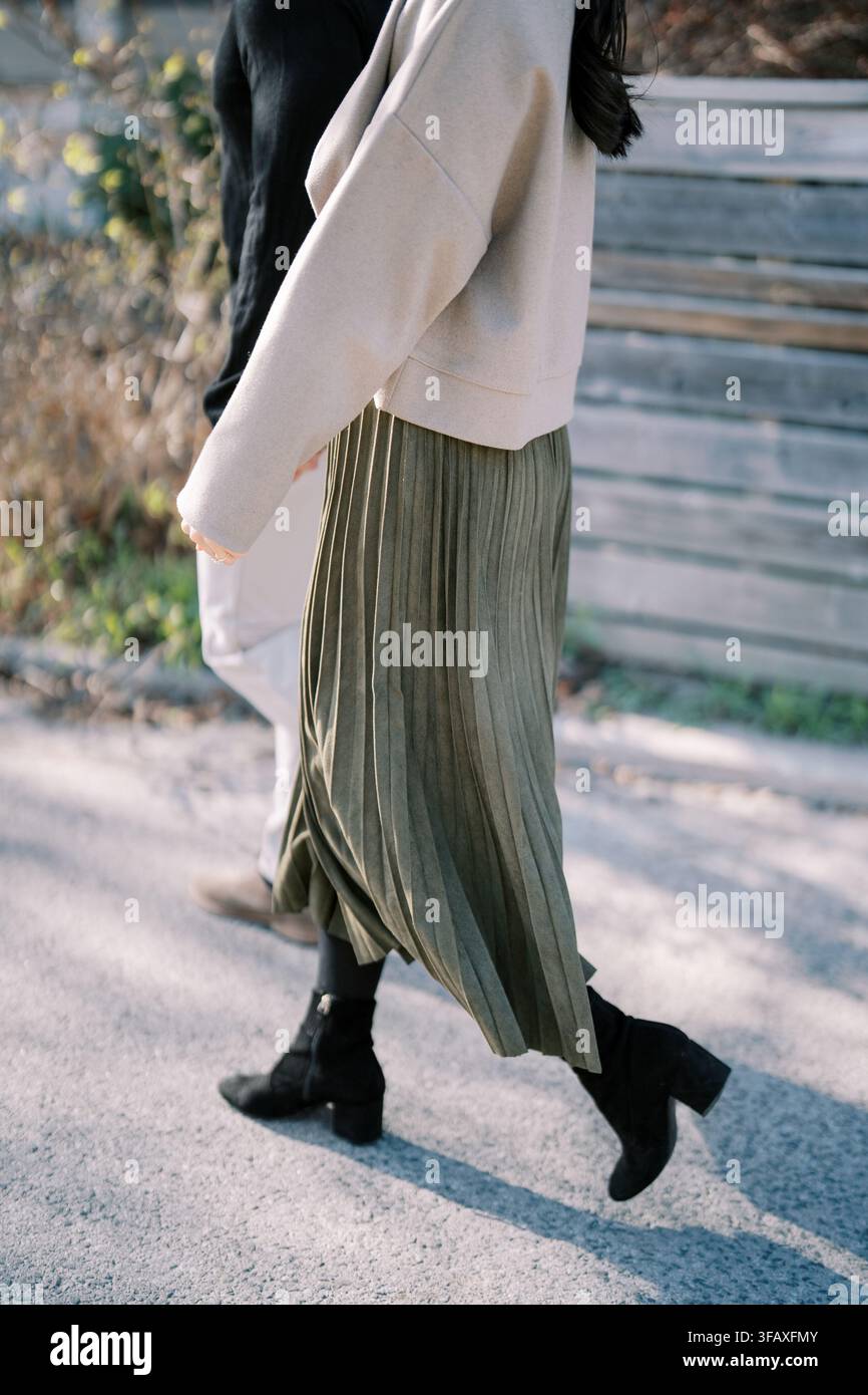 Style de rue en marche avec une jupe plissée verte et un pull beige Banque D'Images