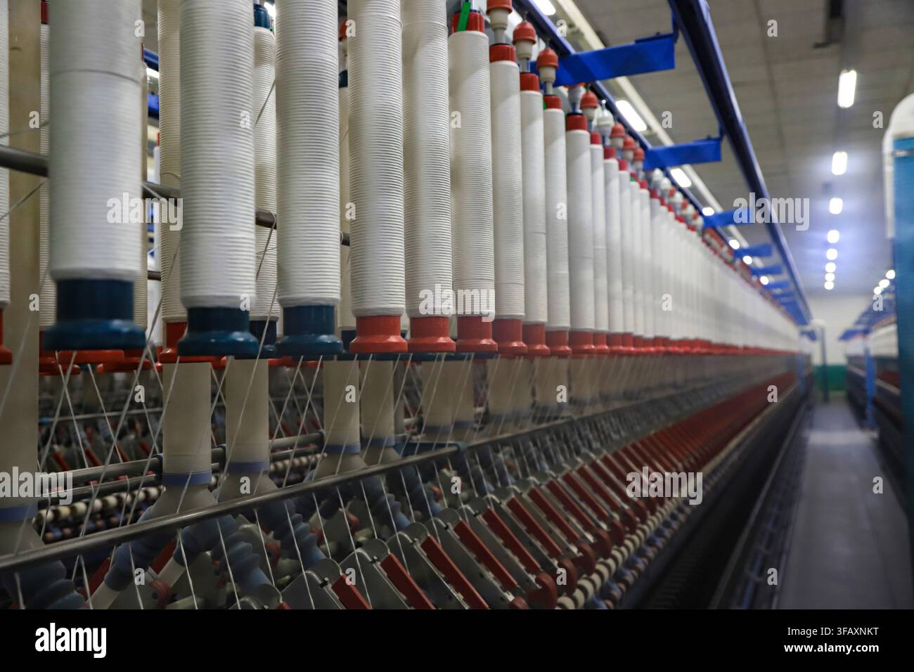 Vue rapprochée de cônes de fil blanc soigneusement disposés dans un atelier de filature, avec des fils s'étendant jusqu'aux machines en dessous, mettant en valeur les détails et l'ordre Banque D'Images