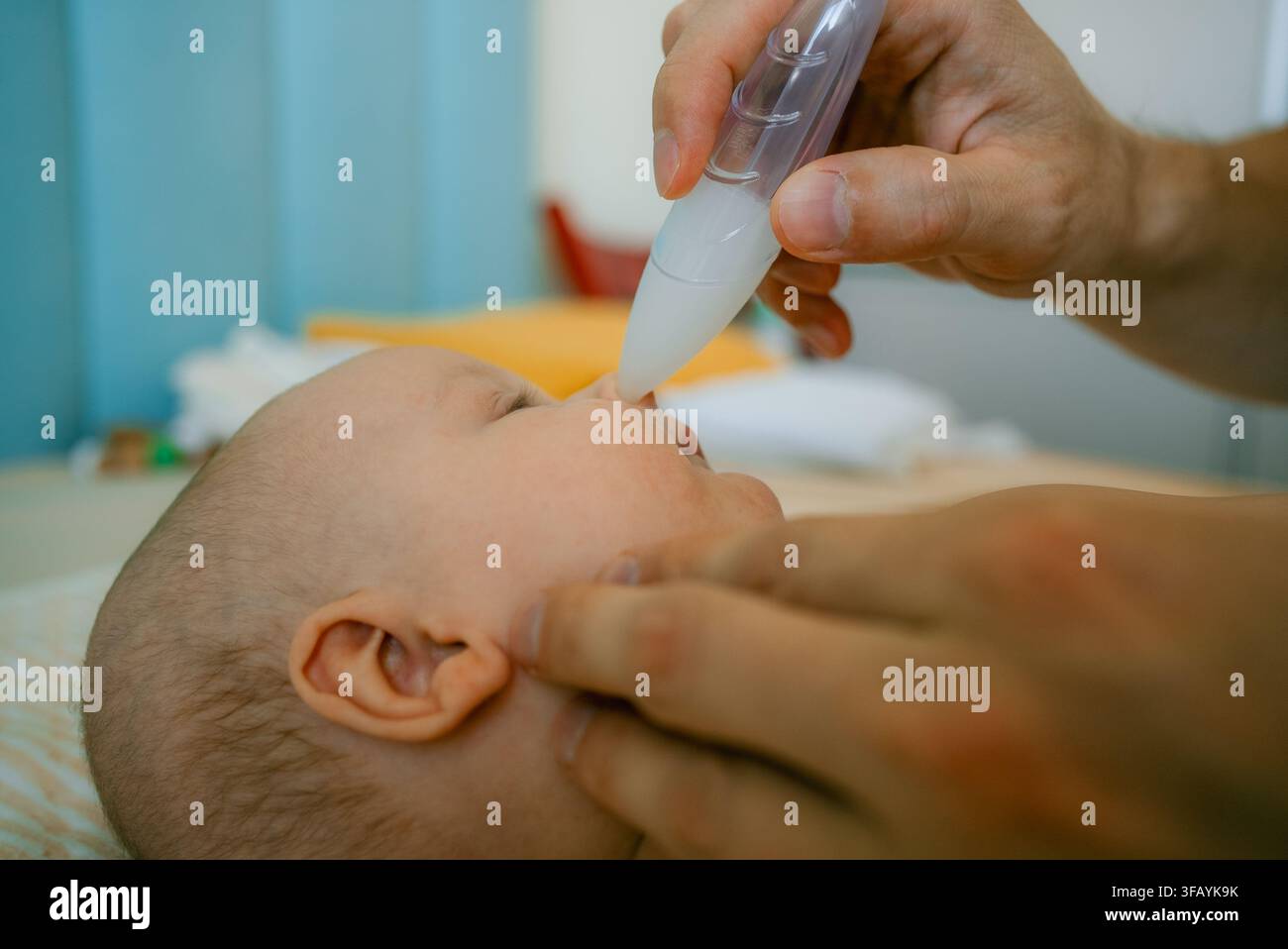 Père tenant un nourrisson sur une table à langer, utilisant un aspirateur nasal pour nettoyer le nez du bébé, extrayant le mucus pour dégager les voies nasales et aider à respirer Banque D'Images