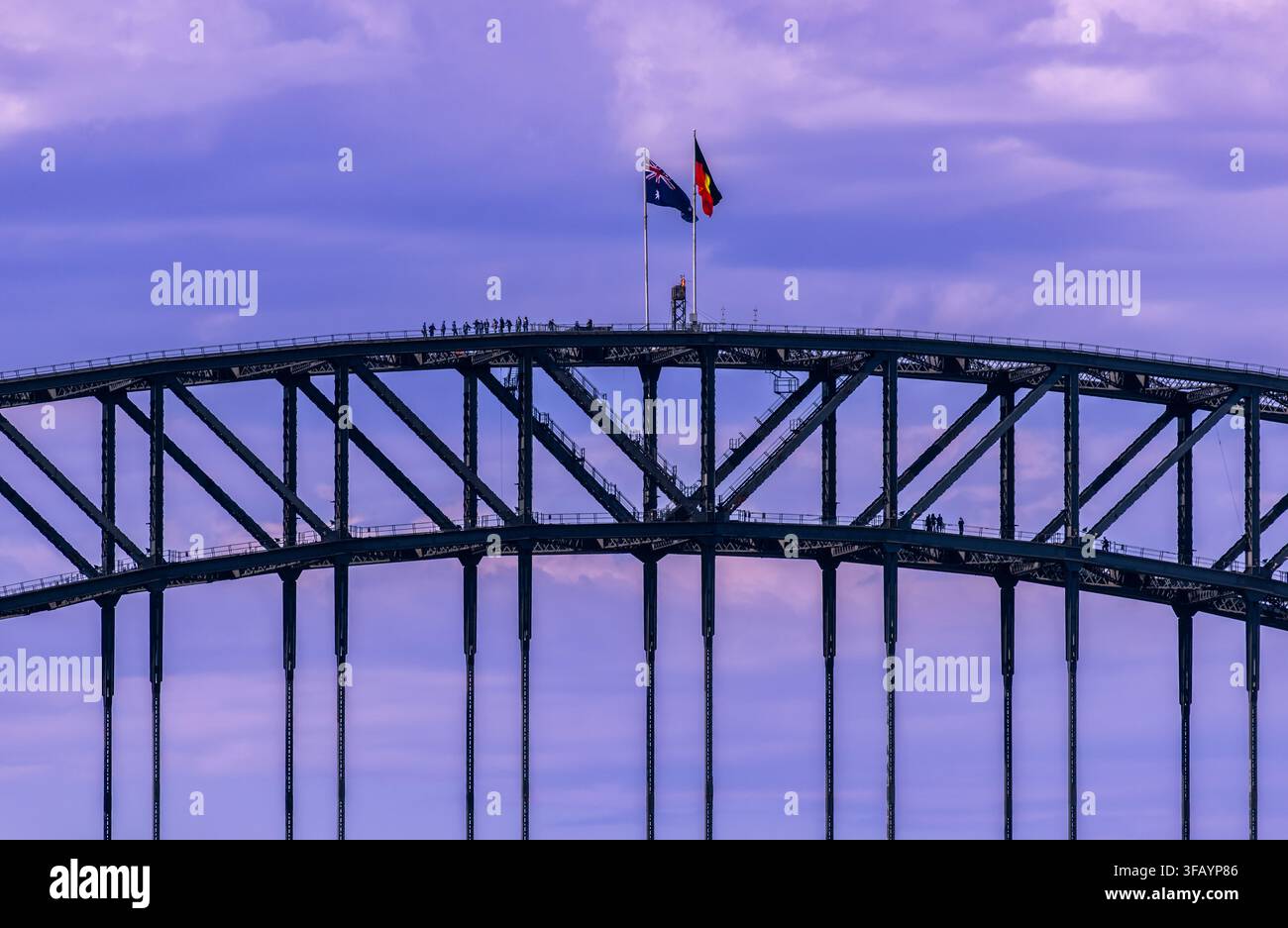 Arc du pont du port de Sydney avec drapeaux australien et aborigène flottant, de minuscules grimpeurs de pont visibles le long de la travée. Banque D'Images