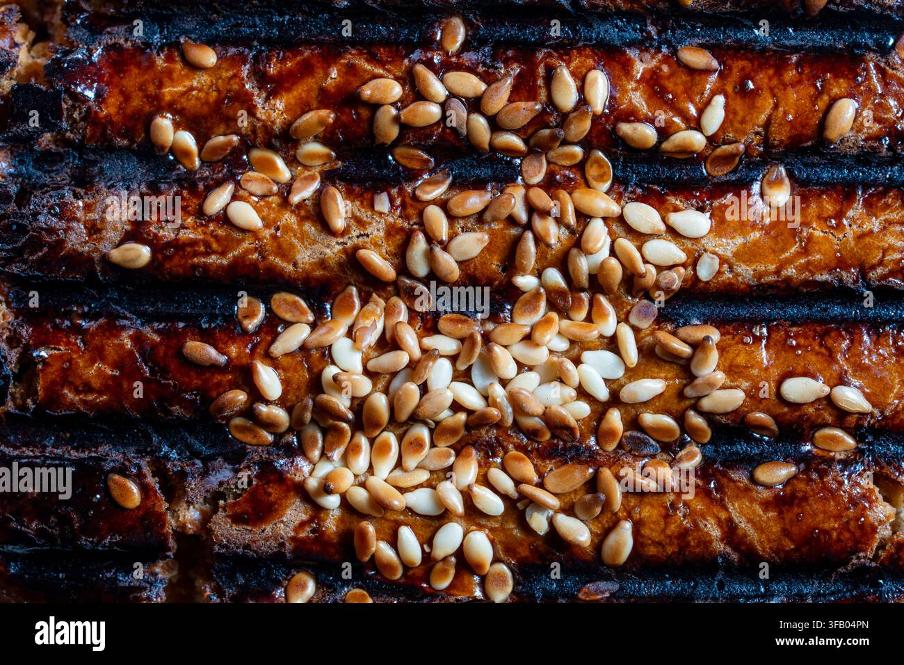 Vue macro de dessus montrant la texture détaillée d'un aliment grillé sombre recouvert de graines de sésame dorées et blanches grillées, gros plan Banque D'Images