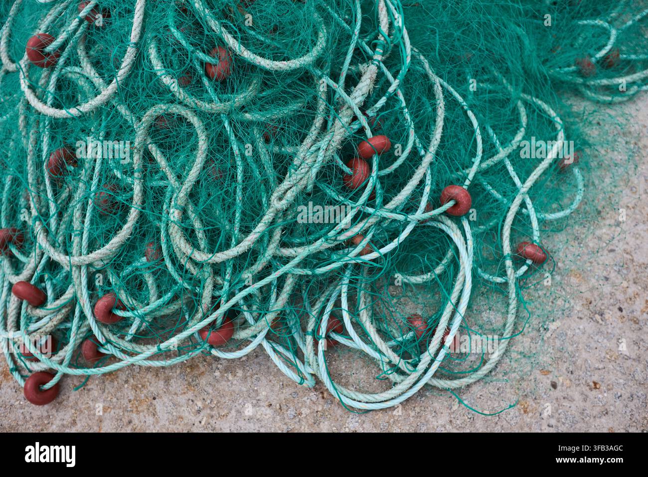 Close-up d'un filet de pêche vert emmêlé avec une corde blanche et une bouée rouge étalé sur une surface de rive rugueuse, montrant un équipement marin traditionnel et co Banque D'Images