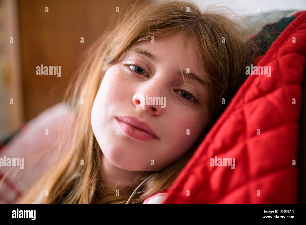 Jeune fille sereine se détend confortablement sur un canapé à la maison, son expression douce encadrée par une lumière naturelle intérieure et un coussin rouge dans une authentique Banque D'Images