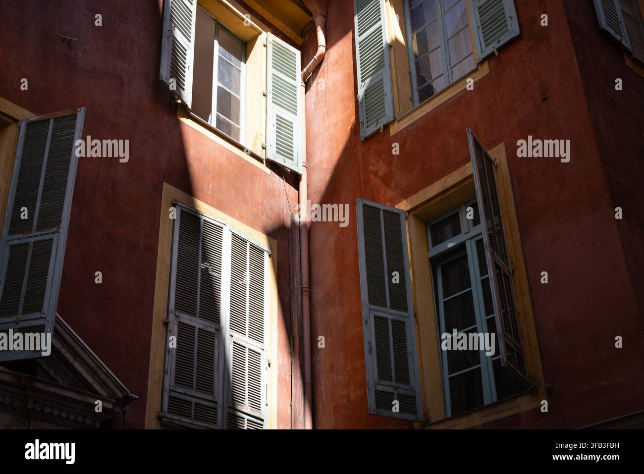 La lumière du soleil illumine les volets pastel et les façades ocre chaudes dans le vieux centre historique de Nice, en France, capturant le charme architectural intime de Banque D'Images