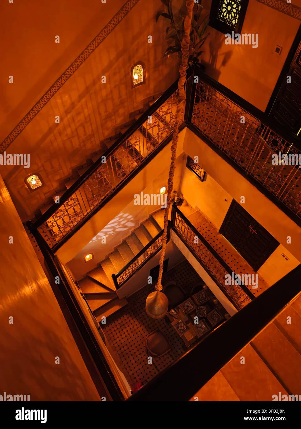 Intérieur marocain traditionnel avec un escalier à plusieurs niveaux, des rampes en fer forgé ornées, des lanternes décoratives et des murs en terre cuite chaude à Marrakech Banque D'Images