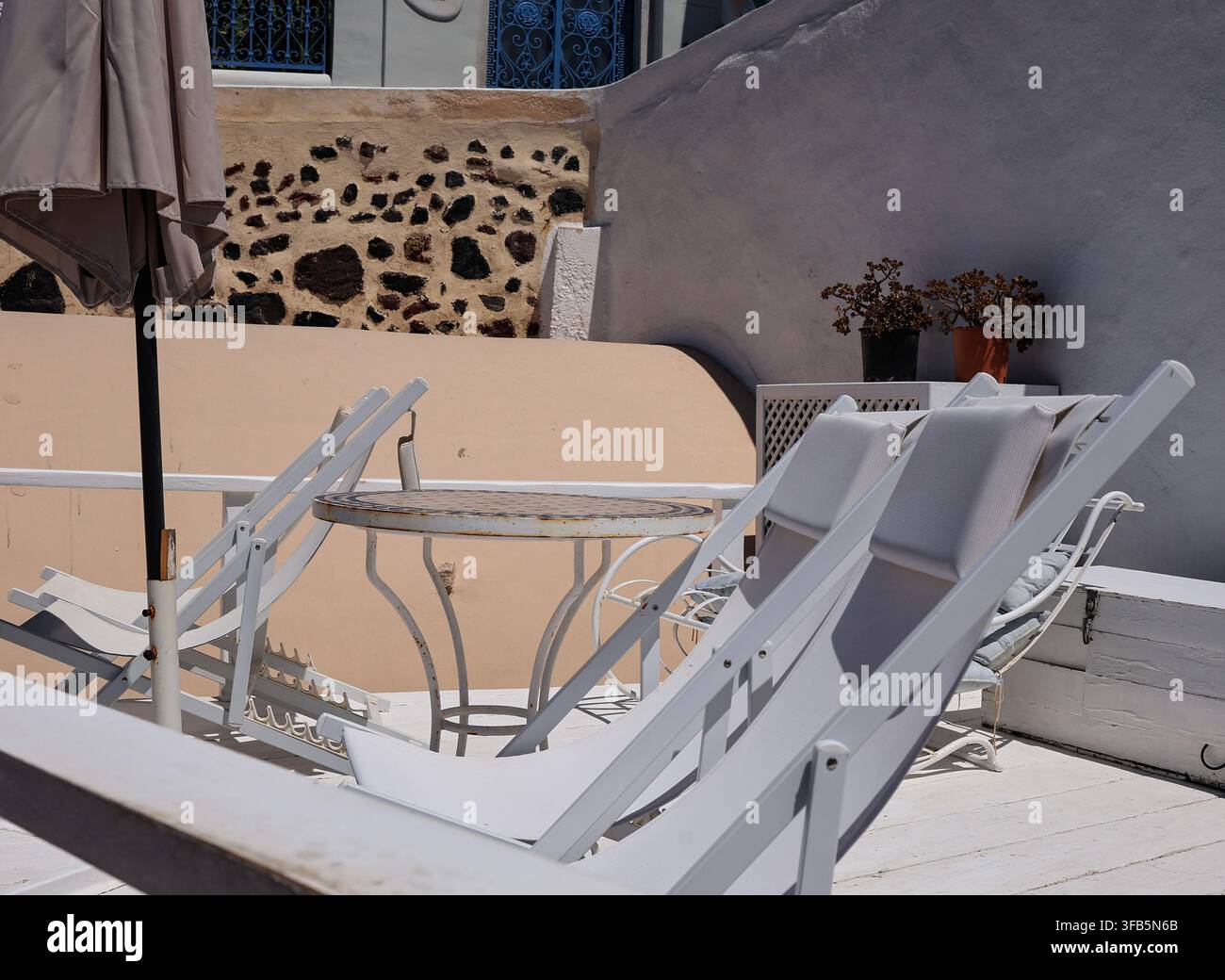Chaises longues et table blanches sur une terrasse avec mur en pierre volcanique, Santorin, Grèce Banque D'Images