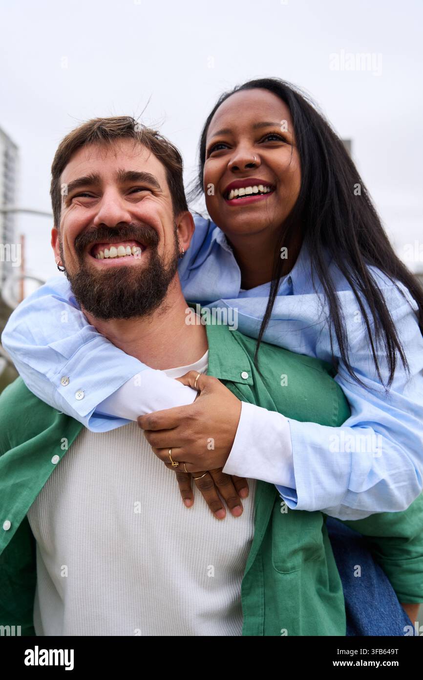 Heureux couple multiracial piggyback et souriant à l'extérieur. Banque D'Images