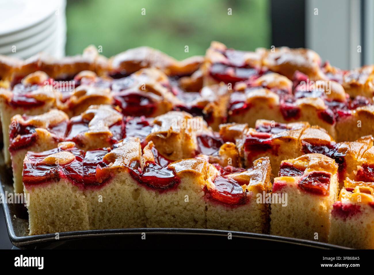 Des morceaux de gâteau rectangulaires sont disposés en rangées organisées. Des fruits cuits reposent à la surface de chaque tranche. Le dessert est arrangé sur un plateau pour le service. Banque D'Images