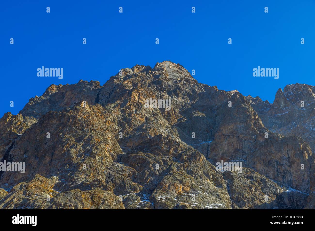 Sommet majestueux avec des pentes escarpées et rocheuses capturé dans une vue basse. Un éclairage dramatique met en valeur les textures de la roche et les plaques de neige Banque D'Images