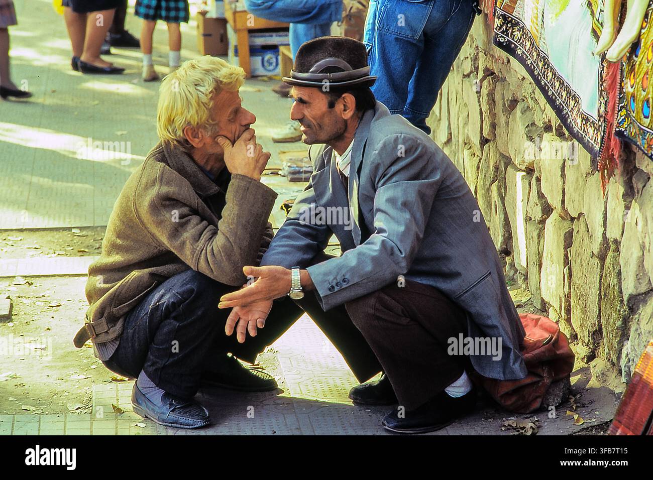 Deux hommes accroupis et discutant avec animation sur un marché de rue animé, scène de vie quotidienne spontanée. Tirana, Albanie, Europe Banque D'Images