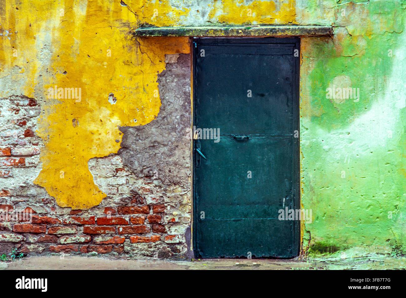 Mur érodé avec peinture jaune et verte écaillée, brique apparente et porte métallique vert foncé, texture de décadence urbaine. Albanie, Europe Banque D'Images