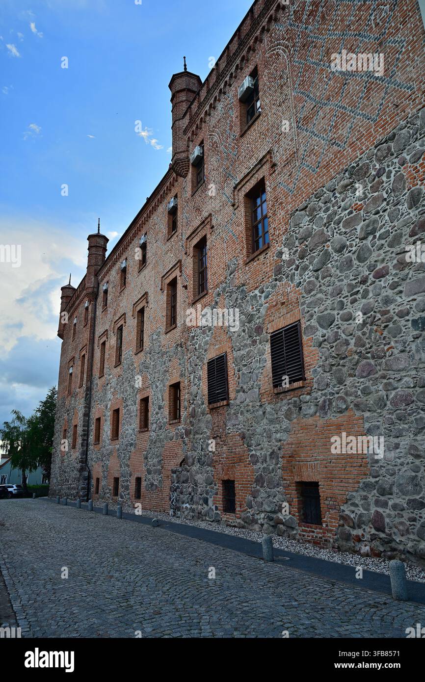 Façade historique de château en briques avec maçonnerie en pierre, tourelles et fenêtres étroites le long d'une rue pavée - Château de Ryn en Mazurie. Banque D'Images