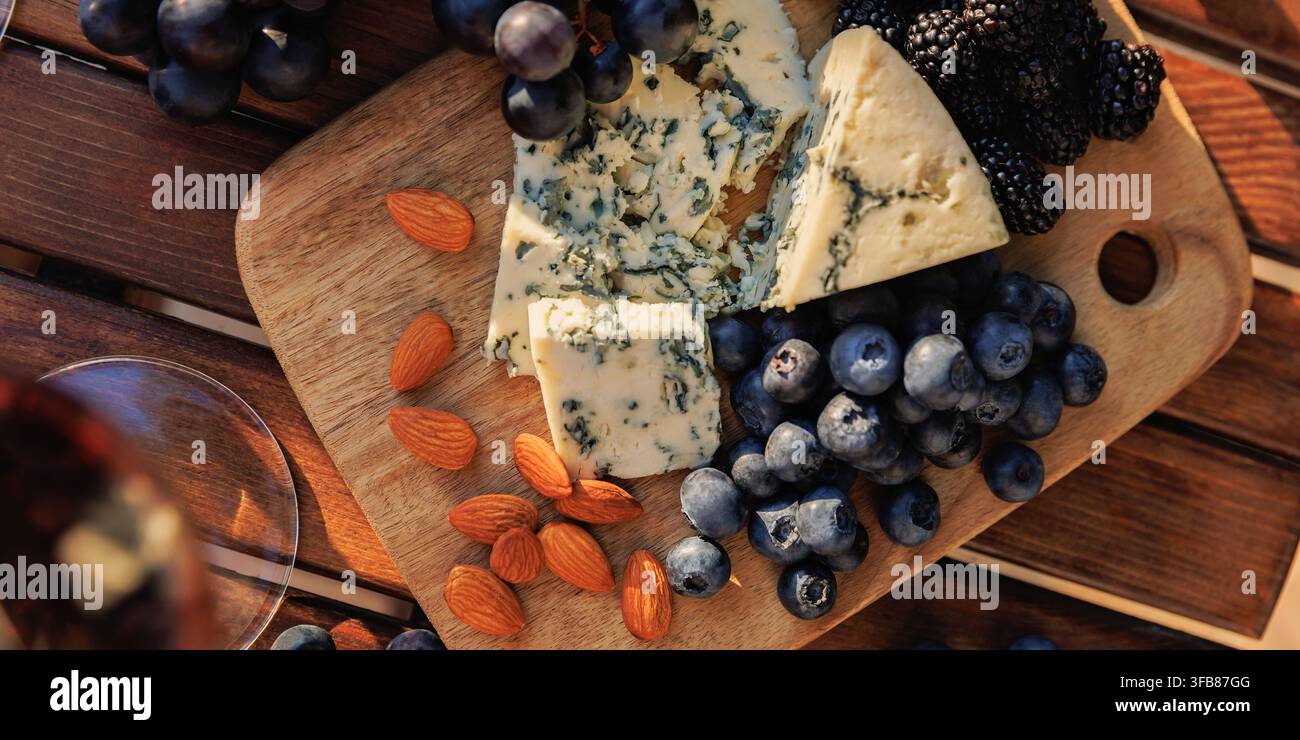 Fromage bleu servi avec des raisins, des myrtilles, des mûres et des amandes sur une planche en bois sous une lumière naturelle Banque D'Images