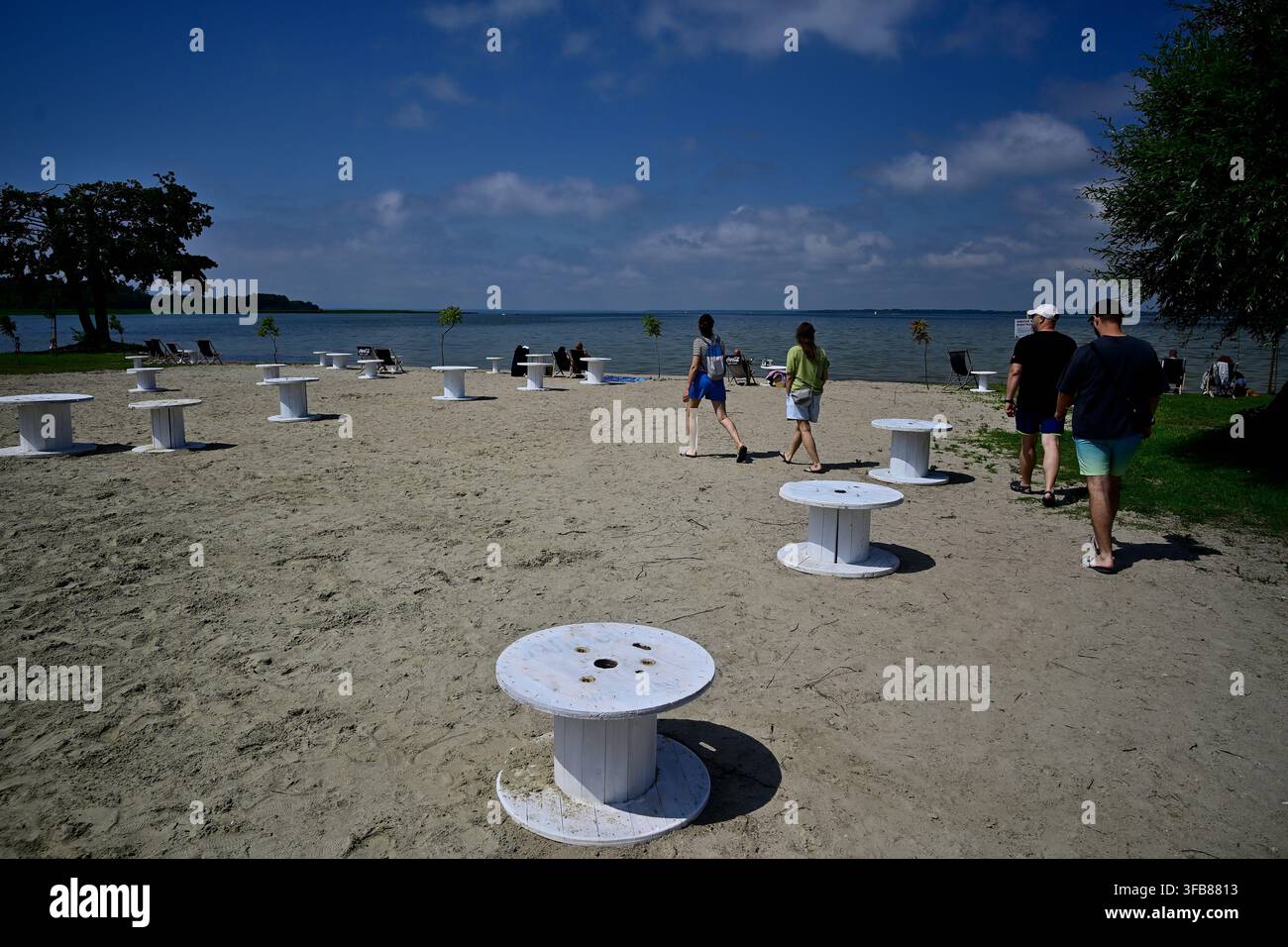 Amis marchant le long de la plage de sable de Sandy Lake avec des tables à bobine blanches et détente estivale - Nowe Guty, lac Śniardwy. Banque D'Images