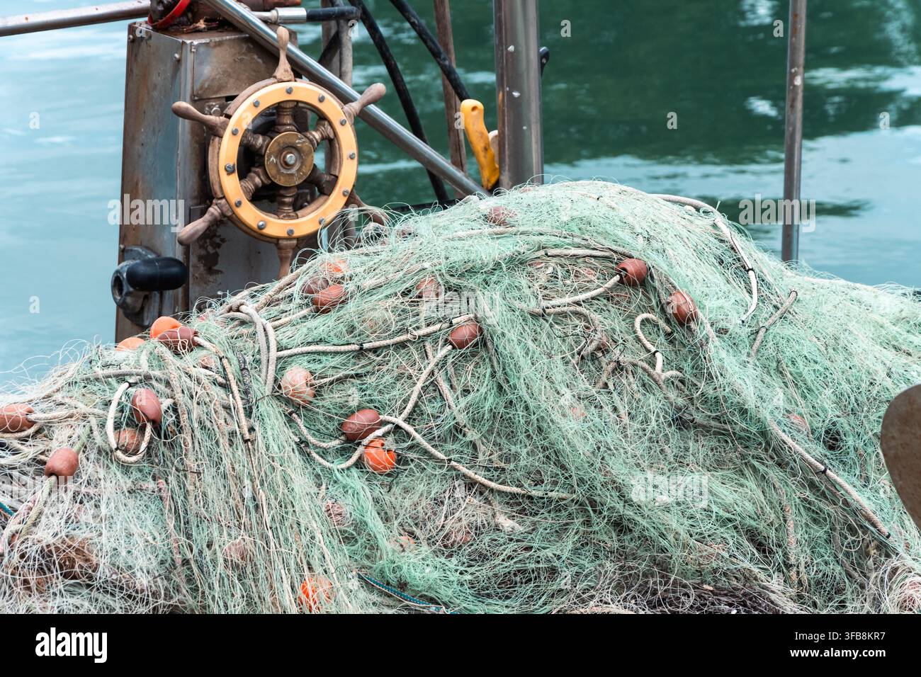 Un grand filet de pêche repose sur le pont d'un bateau à côté d'un volant et d'une eau calme. Banque D'Images
