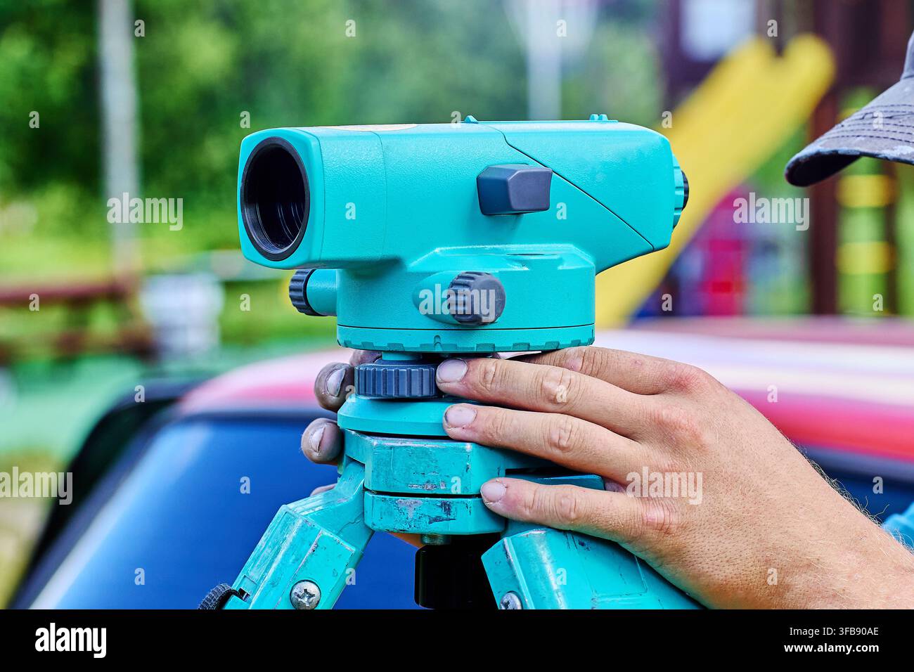 L'équipement de topographie repose sur un trépied tandis que le topographe ajuste le niveau optique pour des mesures horizontales précises et un travail de topographie exact. Banque D'Images
