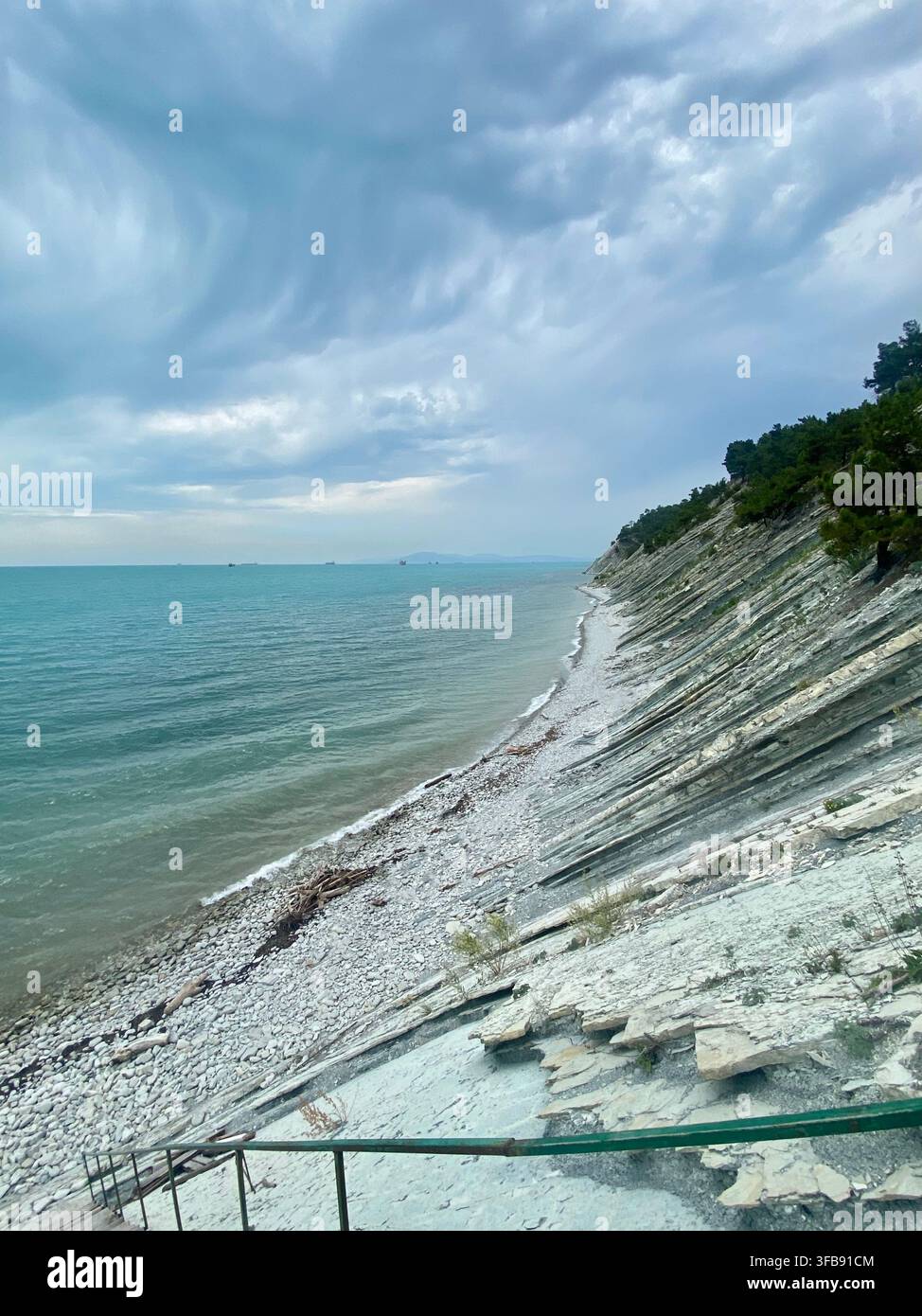 Une côte rocheuse stratifiée s'étend à côté d'une mer turquoise sous un ciel nuageux dramatique. - Image de stock capturée avec un smartphone