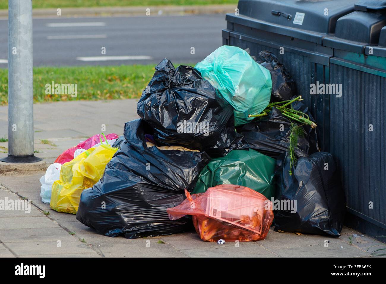 Pile de sacs de déchets ménagers variés laissés à côté des conteneurs à ordures publics sur un trottoir Banque D'Images
