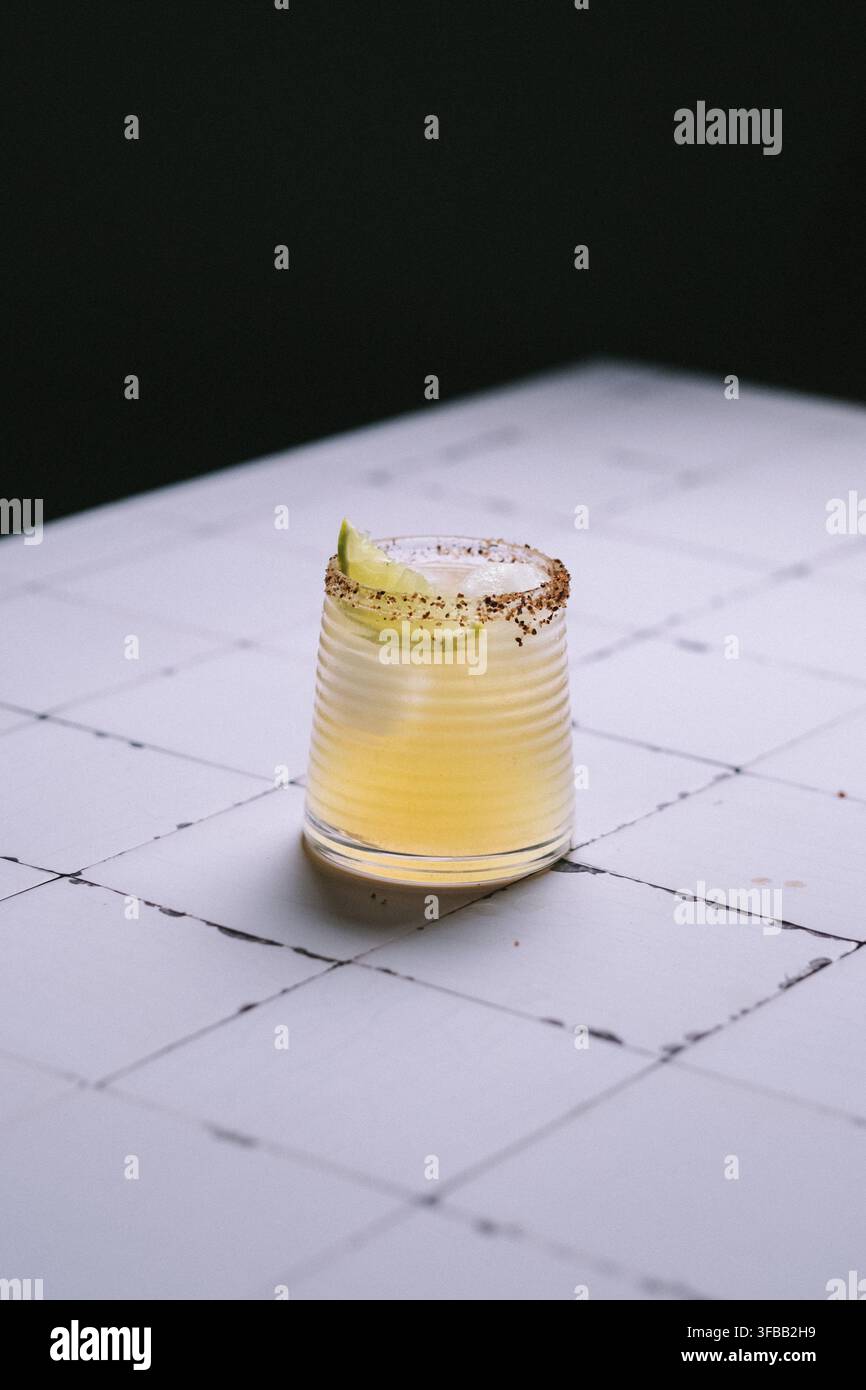 Margarita avec un bord salé au piment et une tranche de citron vert dans un verre cannelé sur une table carrelée blanche, photographie d'ambiance de cocktails mexicains Banque D'Images