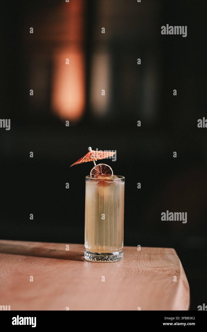 Cocktail Tiki avec un parapluie en papier et un citron vert séché dans un grand verre sur une table en bois dans un bar sombre Banque D'Images