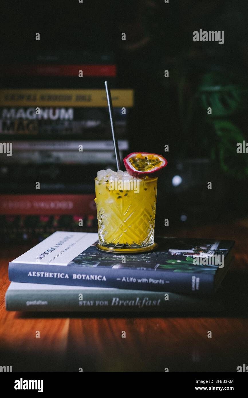 Cocktail de fruits de la passion jaune dans un verre en cristal taillé sur une pile de livres devant une étagère, photographie d'ambiance de boissons Banque D'Images