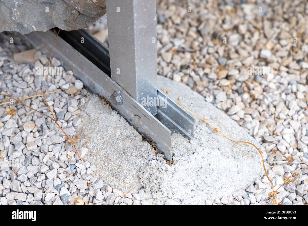 Une vue détaillée d'un poteau de support en métal fixé dans une fondation en béton, entouré de petites pierres et de végétation sèche Banque D'Images