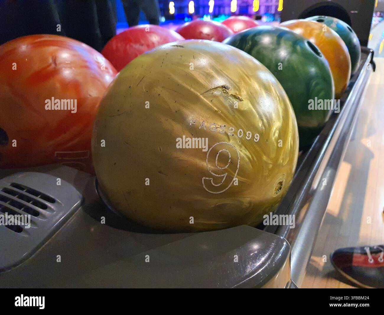 Vue rapprochée de plusieurs boules de bowling colorées alignées sur un retourneur de boules dans une salle de bowling intérieure. Le premier plan présente une usure Banque D'Images