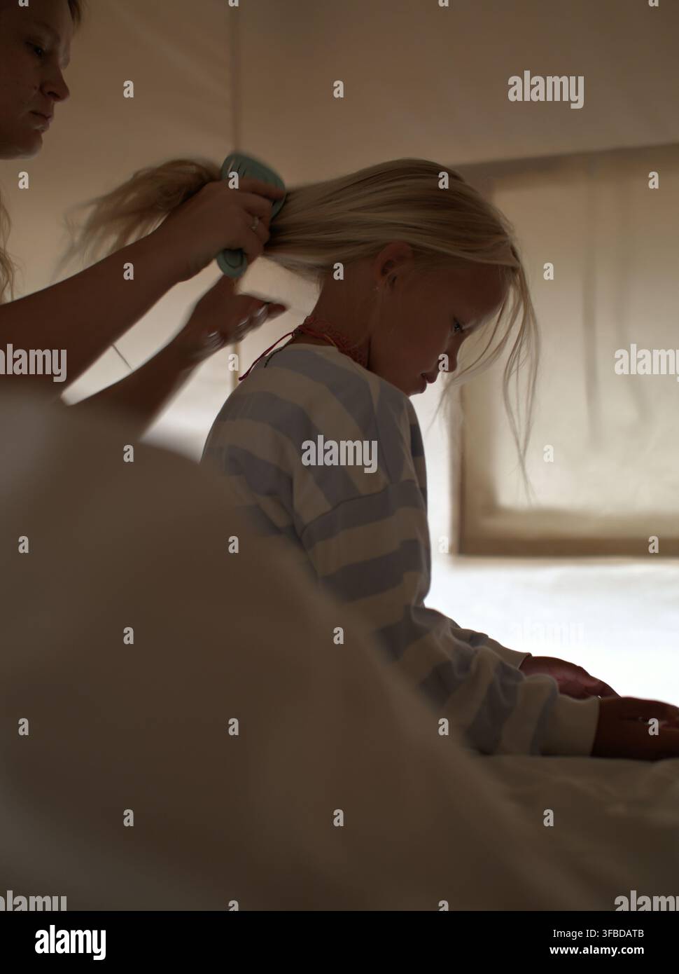 Femme brosse les longs cheveux blonds de sa fille dans une tente Banque D'Images