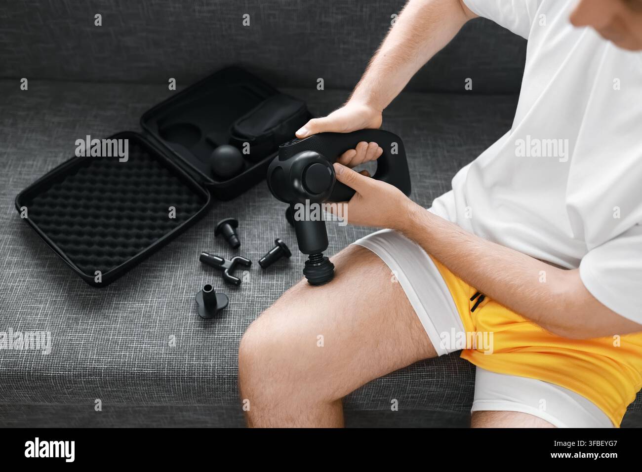 Homme utilisant une perceuse de massage sur sa cuisse pour la récupération post-entraînement et le soulagement des tensions musculaires. Auto-soins à domicile, thérapie par percussion, libération myofasciale et p Banque D'Images