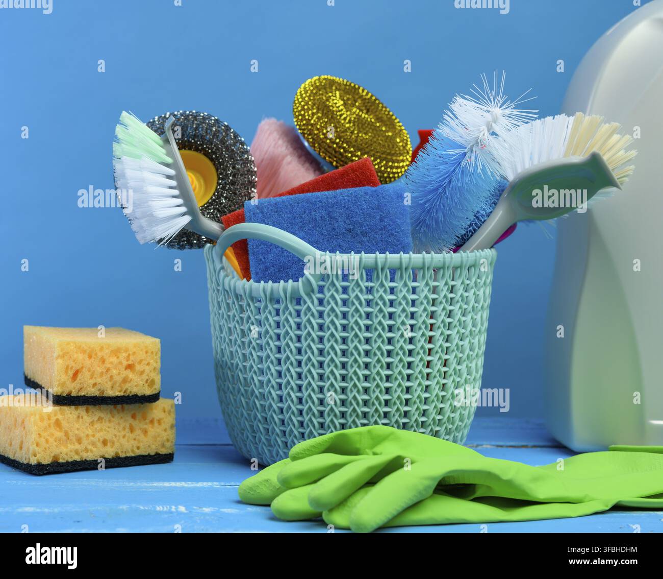 panier en plastique bleu avec brosses, éponges et gants en caoutchouc pour le nettoyage, fond bleu Banque D'Images