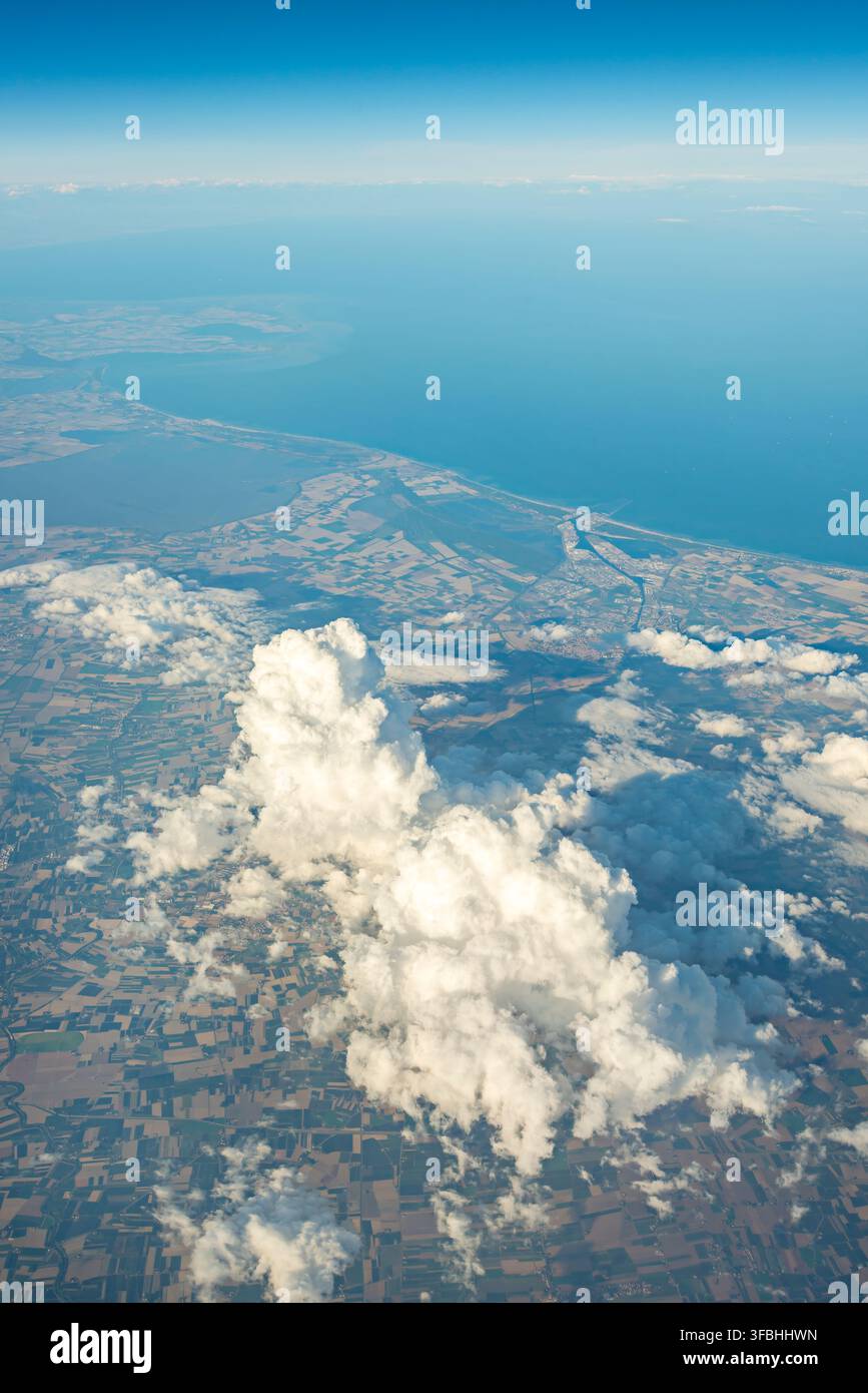Nuages cumulus imposants s'élevant au-dessus d'un patchwork côtier de terres agricoles rencontrant la mer Banque D'Images