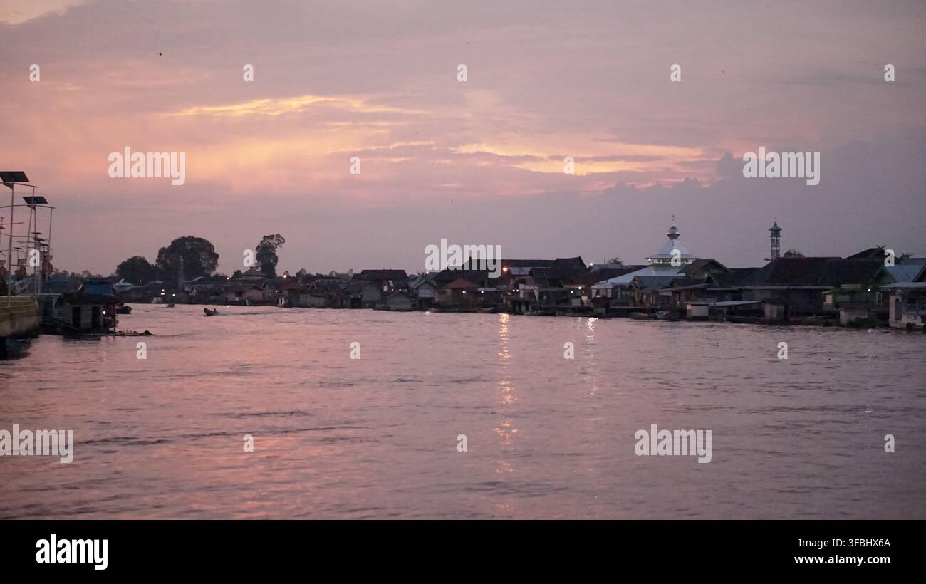 De magnifiques teintes de coucher de soleil se reflètent sur une rivière tranquille près d'un village sur pilotis et d'une mosquée Banque D'Images