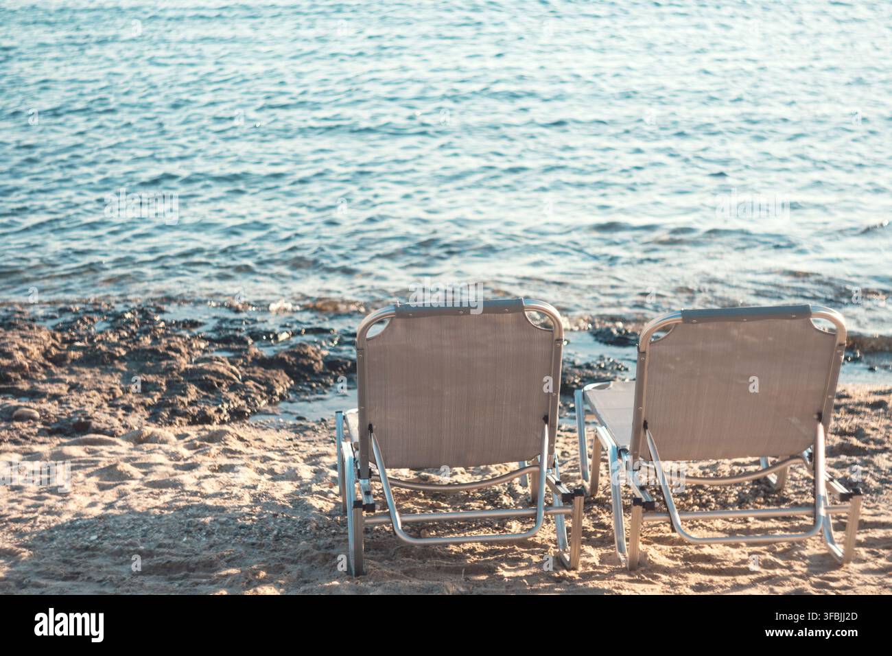 Deux transats vides posés sur une plage de sable face à l'eau bleue de la mer, capturés en Grèce. Banque D'Images