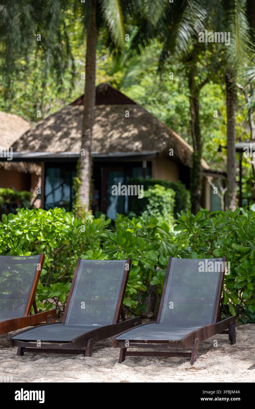 PLAGE DE TUBKAEK, THAÏLANDE — 18 FÉVRIER 2026 : Deux transats vides sont posés devant des bungalows de resort en paille au milieu d'une végétation tropicale sur la côte de Krabi. Banque D'Images
