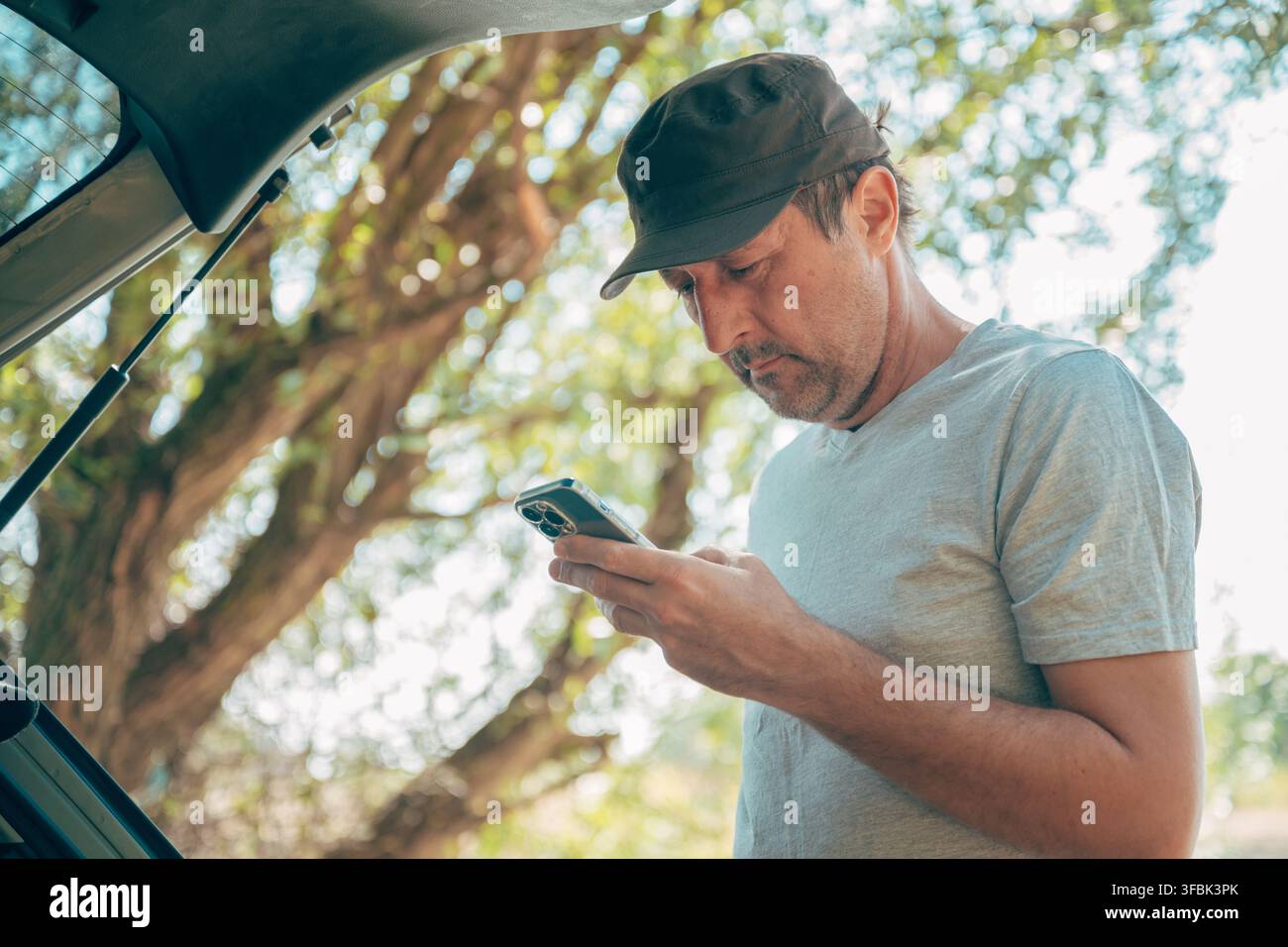Conducteur vérifiant les cartes de route en ligne et les messages sur un smartphone près du hayon ouvert de son véhicule. Connexion moderne pour les voyages, technologie de voyage, numérique Banque D'Images