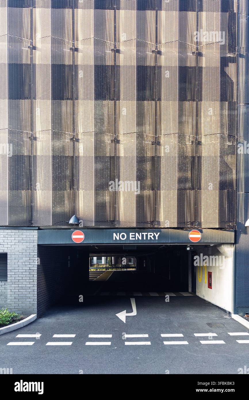 Sortie d’un parking marqué « Entrée interdite », sous un bâtiment commercial moderne, avec des marquages routiers directionnels et un revêtement architectural à motifs - Image de stock capturée avec un smartphone