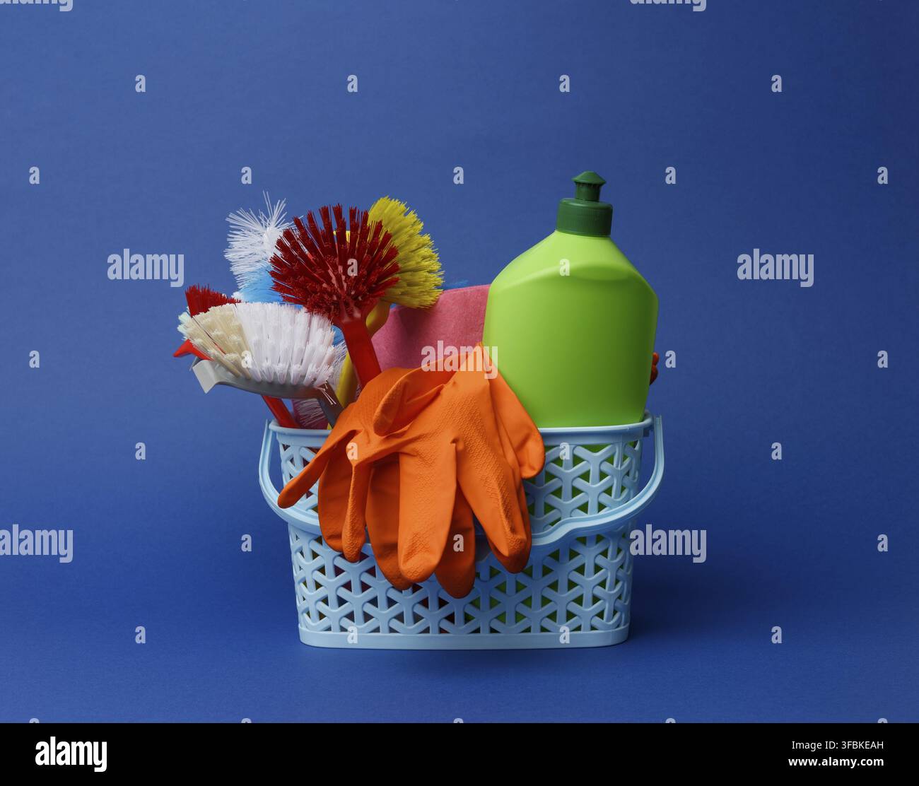 panier en plastique bleu avec brosses, éponges et gants en caoutchouc pour le nettoyage, fond bleu Banque D'Images
