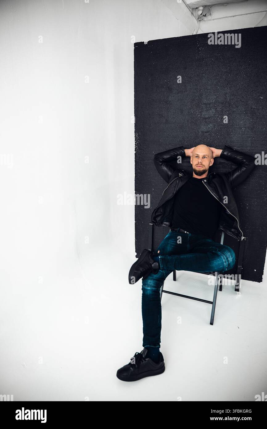 Un homme se détend sur une chaise avec les bras derrière la tête dans un cadre de studio. Banque D'Images