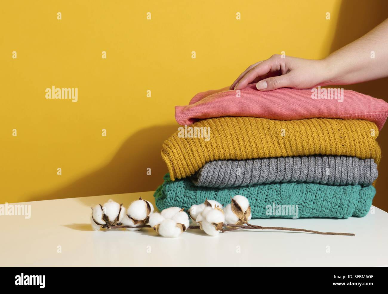 Femme tenant une pile de chandails tricotés pliés sur un fond jaune. Laver les vêtements, nettoyer les choses Banque D'Images