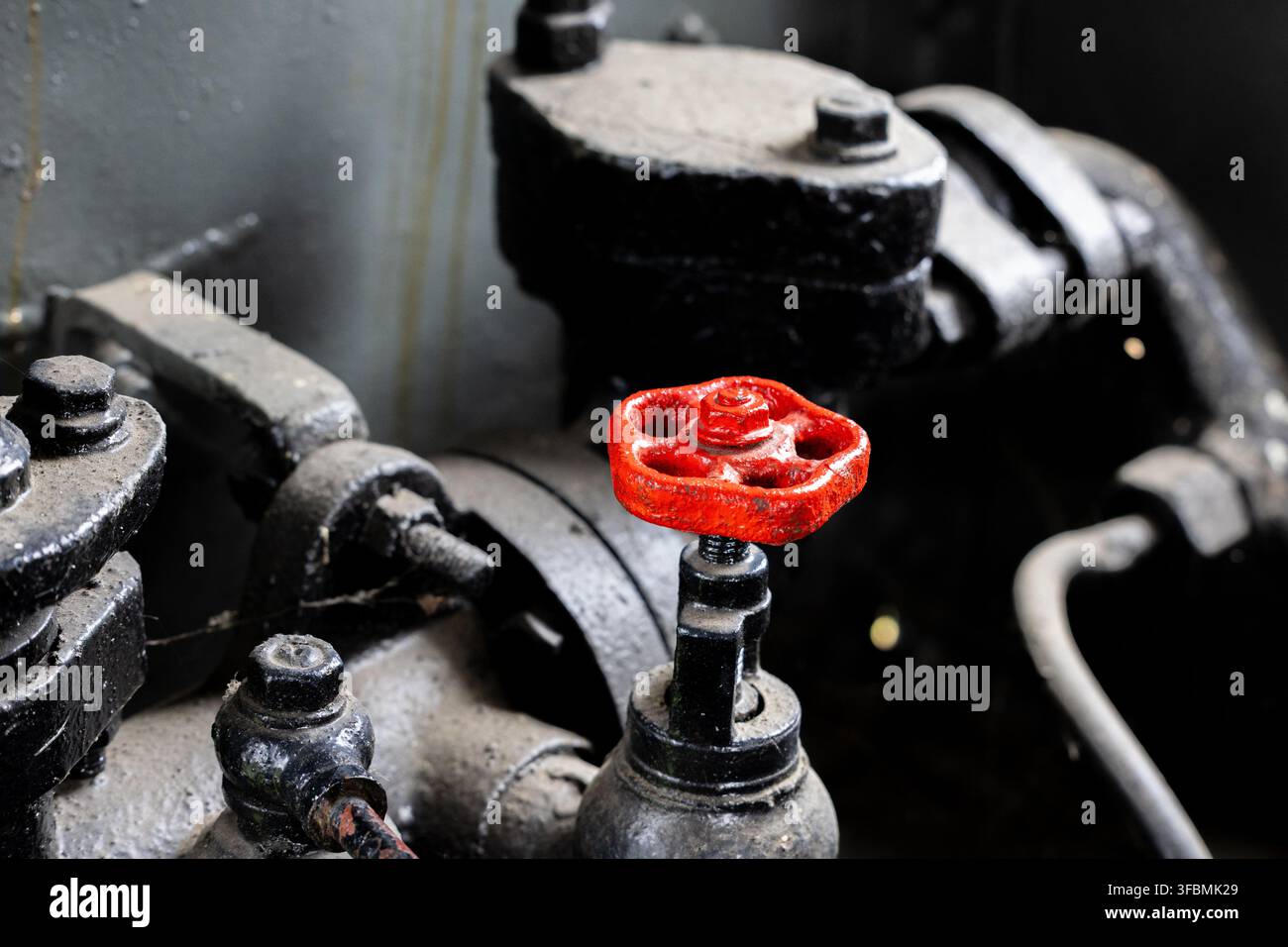 Valve avec une manette et un bouton rouges uniques est montée sur la tuyauterie de la chaudière. Les boulons, rivets, raccords et la corrosion de surface sont visibles en gros plan. Banque D'Images
