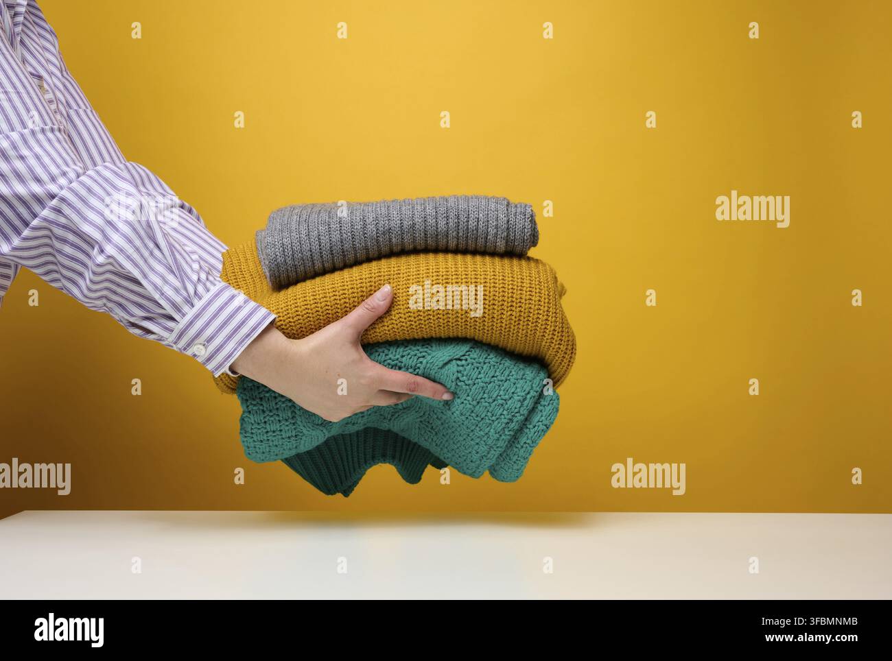 Femme tenant une pile de chandails tricotés pliés sur un fond jaune. Laver les vêtements, nettoyer les choses Banque D'Images