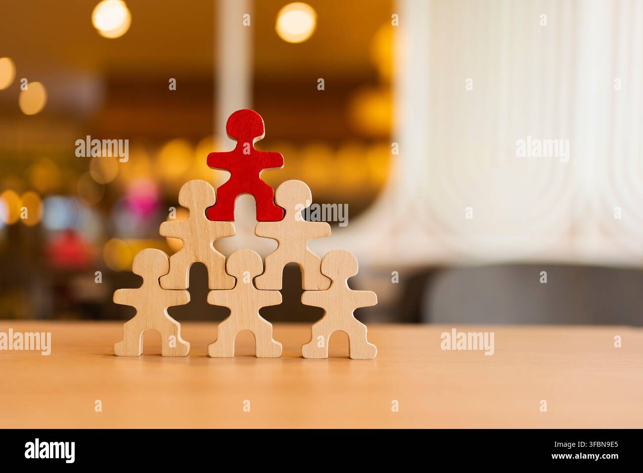 Concept de leadership et de gestion d'entreprise avec une figure en bois rouge au sommet d'une structure pyramidale humaine sur une table pour la promotion de carrière, hiérarchie d'entreprise Banque D'Images