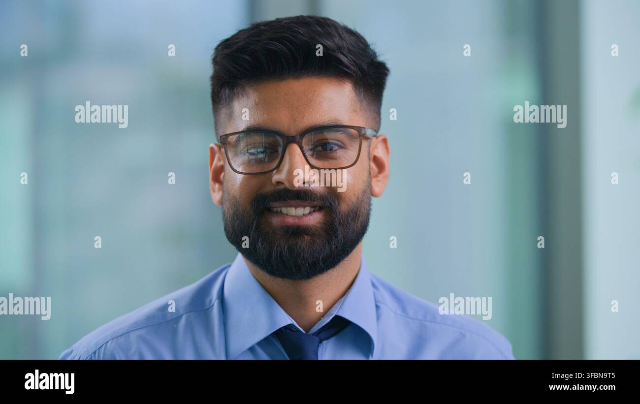 Gros plan d'un homme d'affaires musulman indien confiant et optimiste souriant et regardant la caméra dans une agence de marketing, homme d'affaires arabe avec des lunettes, souriant heureux dans Banque D'Images