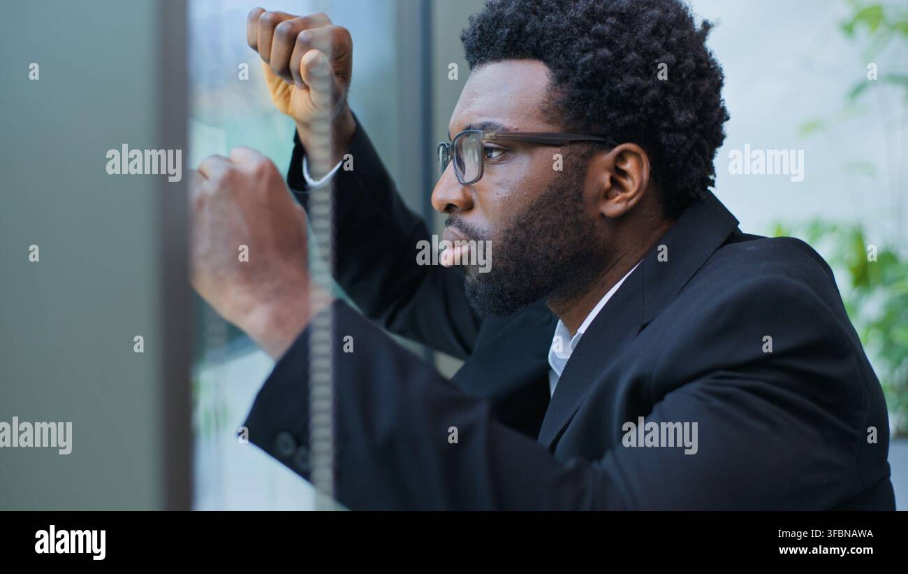 Gros plan d'un homme d'affaires afro-américain inquiet, agacé, stressé, appuyé contre un mur de fenêtre, souffrant de chagrin, homme d'affaires surmené qui souffre Banque D'Images