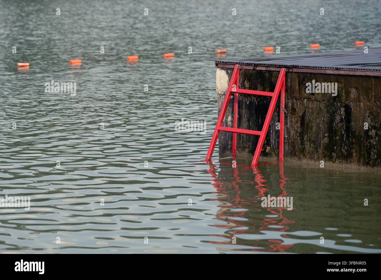 Une vue sombre et atmosphérique d'un lac sombre avec des bouées de sécurité et un escalier en métal rouge. Concept d'accident aquatique, d'incident d'urgence, de risque et de sauvetage Banque D'Images