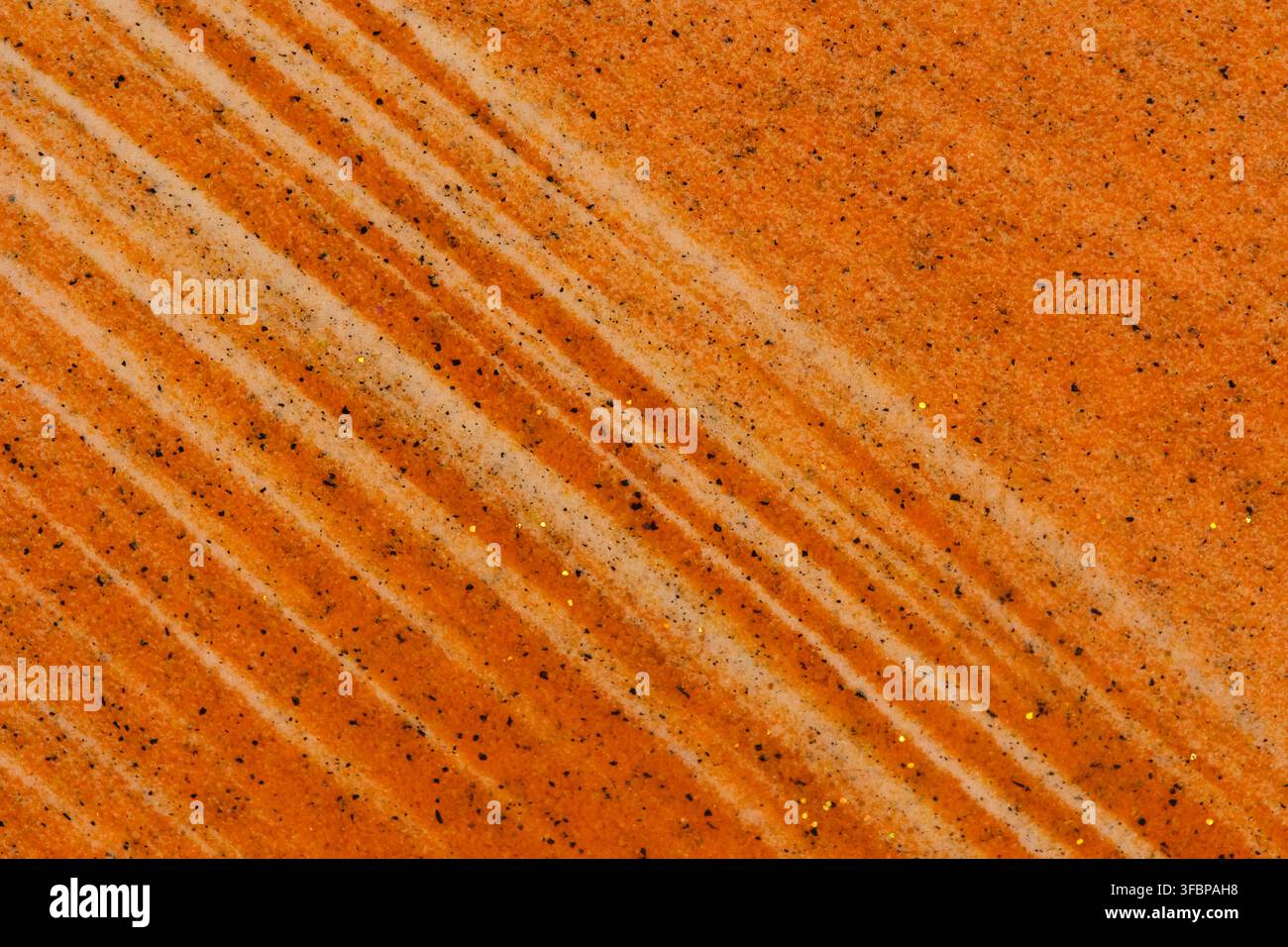 Grossissement diagonal d'une surface texturée orange avec des taches sombres et des particules de paillettes dorées scintillantes Banque D'Images