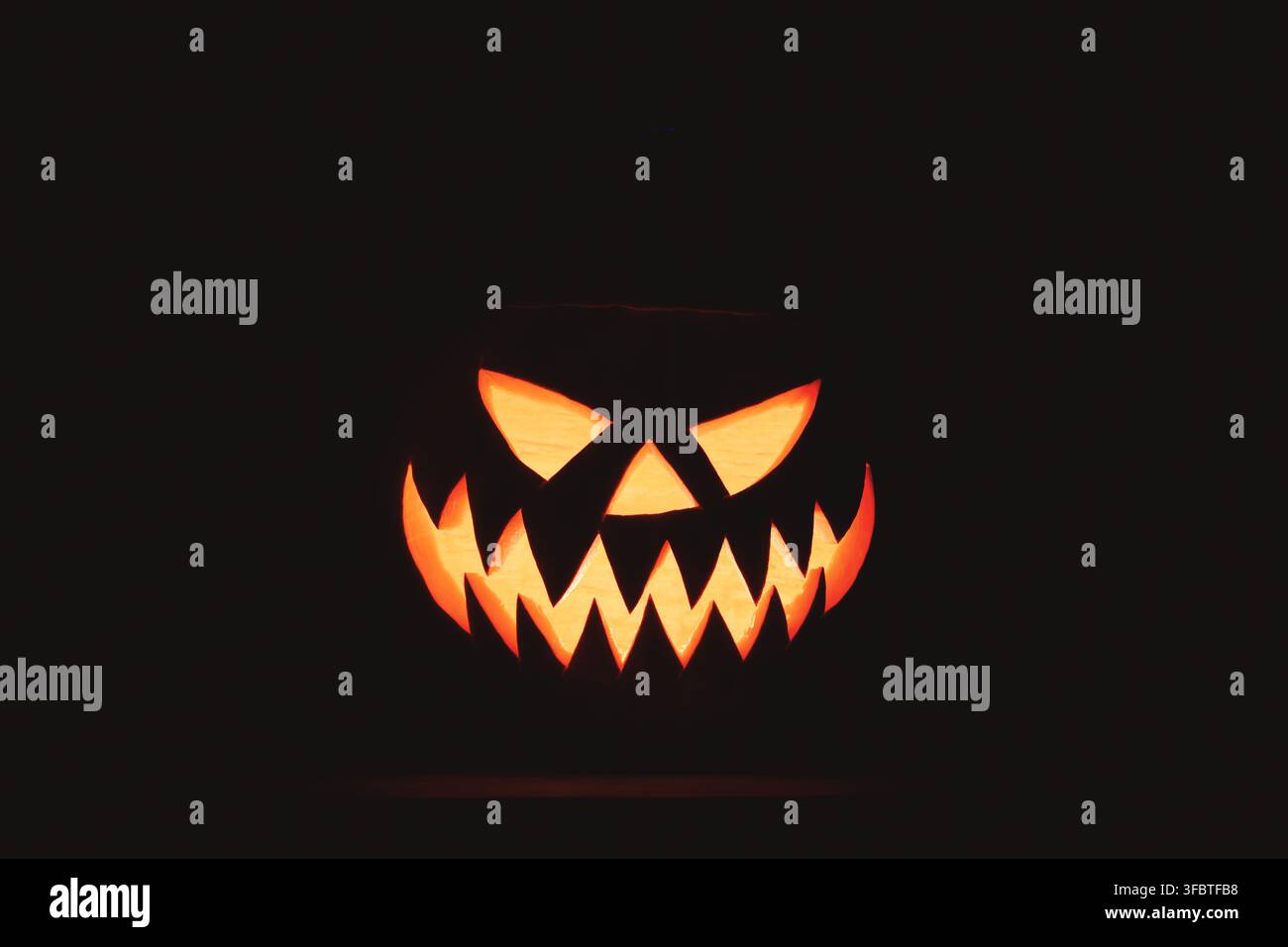 Visage de jack-o'-lanterne lumineux émergeant de l'obscurité avec des dents acérées et une expression maléfique. Fond d'Halloween mettant en vedette une citrouille illuminée et un espace négatif noir dramatique Banque D'Images