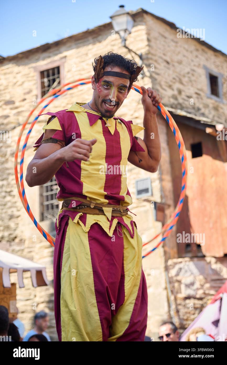 Artiste vêtu d'un costume médiéval coloré, portant du maquillage facial et un couvre-chef, tenant un cerceau de hula hoop et gesticulant vers le spectateur tout en participant à une reconstitution historique Banque D'Images