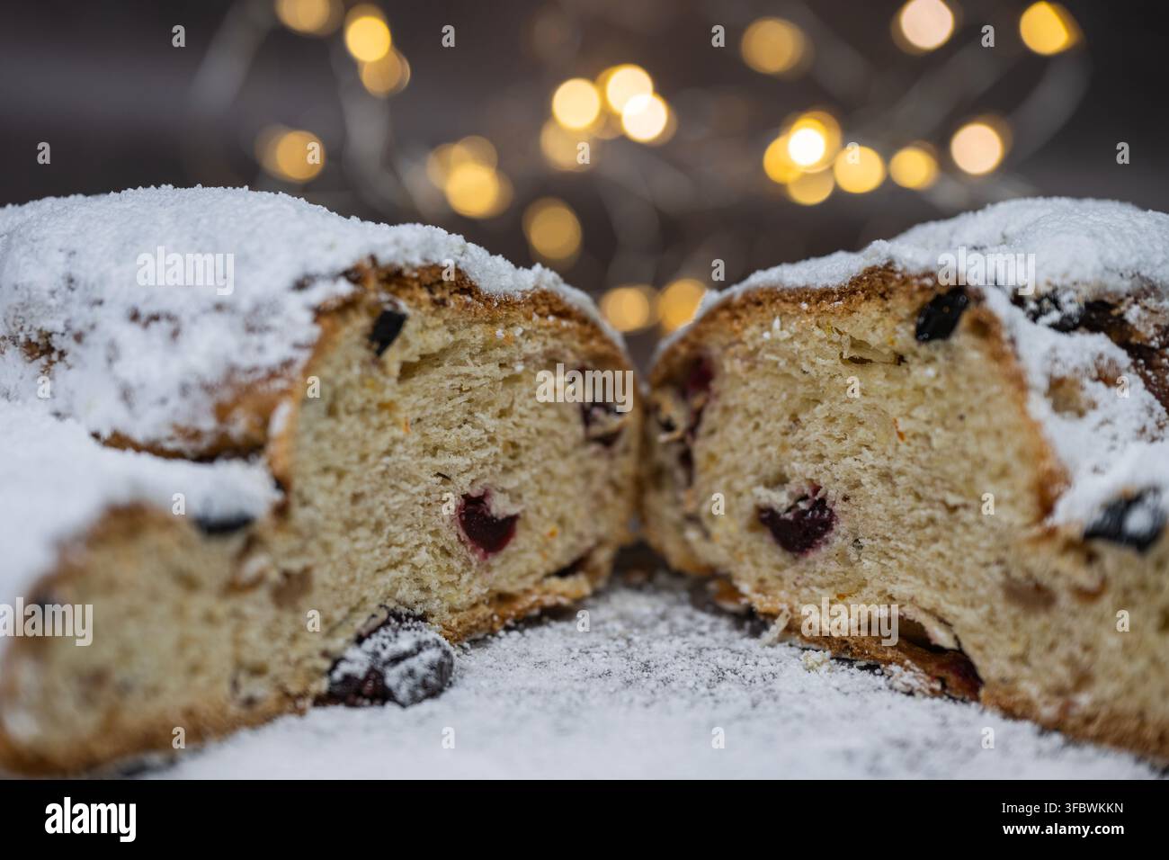 Un gros plan de deux moitiés d'un pain de fruits traditionnel de Noël (stollen) saupoudré de sucre glace sur un fond sombre avec des lumières bokeh douces Banque D'Images